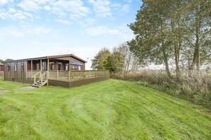 A single-story wooden building with a porch, a fenced deck, and a grassy yard.
