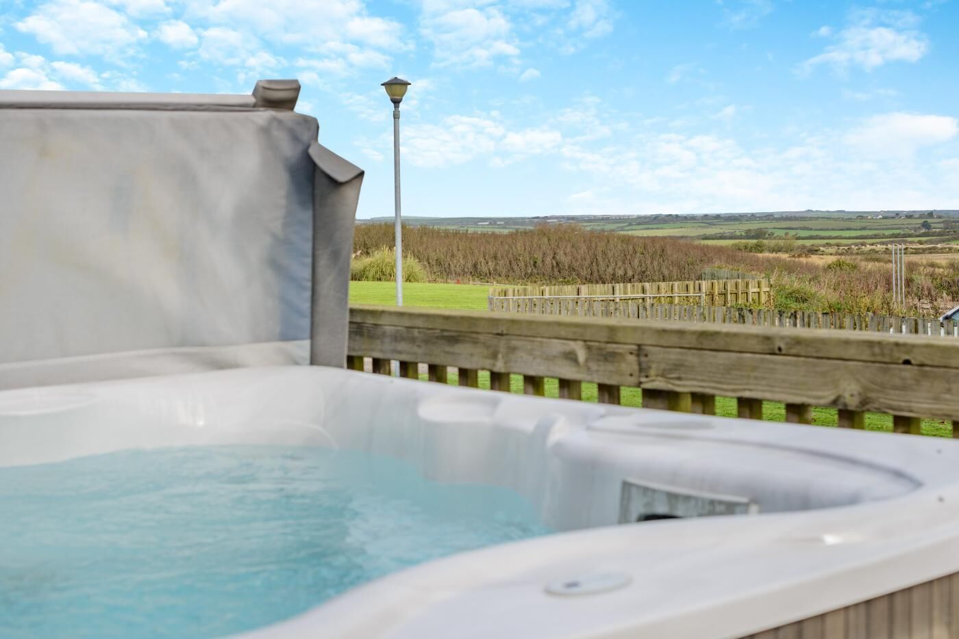 Un jacuzzi con terraza de madera y farola, con vistas a un campo cubierto de césped.