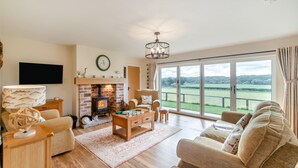 Un salon spacieux doté d’une cheminée, de sièges confortables et d’une grande fenêtre offrant une vue sur la campagne.