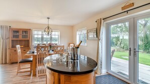 Une salle à manger spacieuse avec une table ronde, des chaises en bois et un lustre. Une bouteille de champagne est posée sur la table, et une grande porte-fenêtre coulissante donne accès à un espace extérieur.
