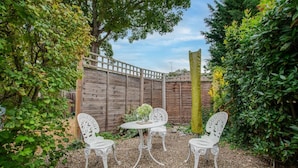 Eine Gartenpatio mit Holzzaun, weißen schmiedeeisernen Stühlen und einem kleinen Tisch.
