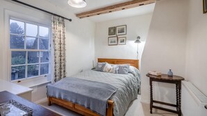 Ein Schlafzimmer mit Bett, Fenster, Nachttisch und Lampe.