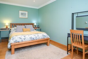 Ein Schlafzimmer mit einem Bett, Nachttischen, einem Sessel, einem Schreibtisch und einem gerahmten Bild an der Wand.