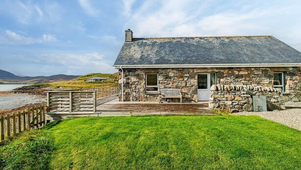 Una casa de piedra con terraza de madera, un banco y vistas al mar.
