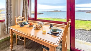 A dining table with breakfast items, a view of the sea, and a window with red frames. - 1 Bed in Reef (oc-r30134) (Uig)