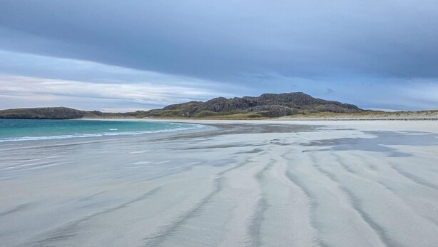 A beach with a wide sandy shore, calm water, and distant rocky hills under a cloudy sky. - 1 Bed in Reef (oc-r30134) (Uig)