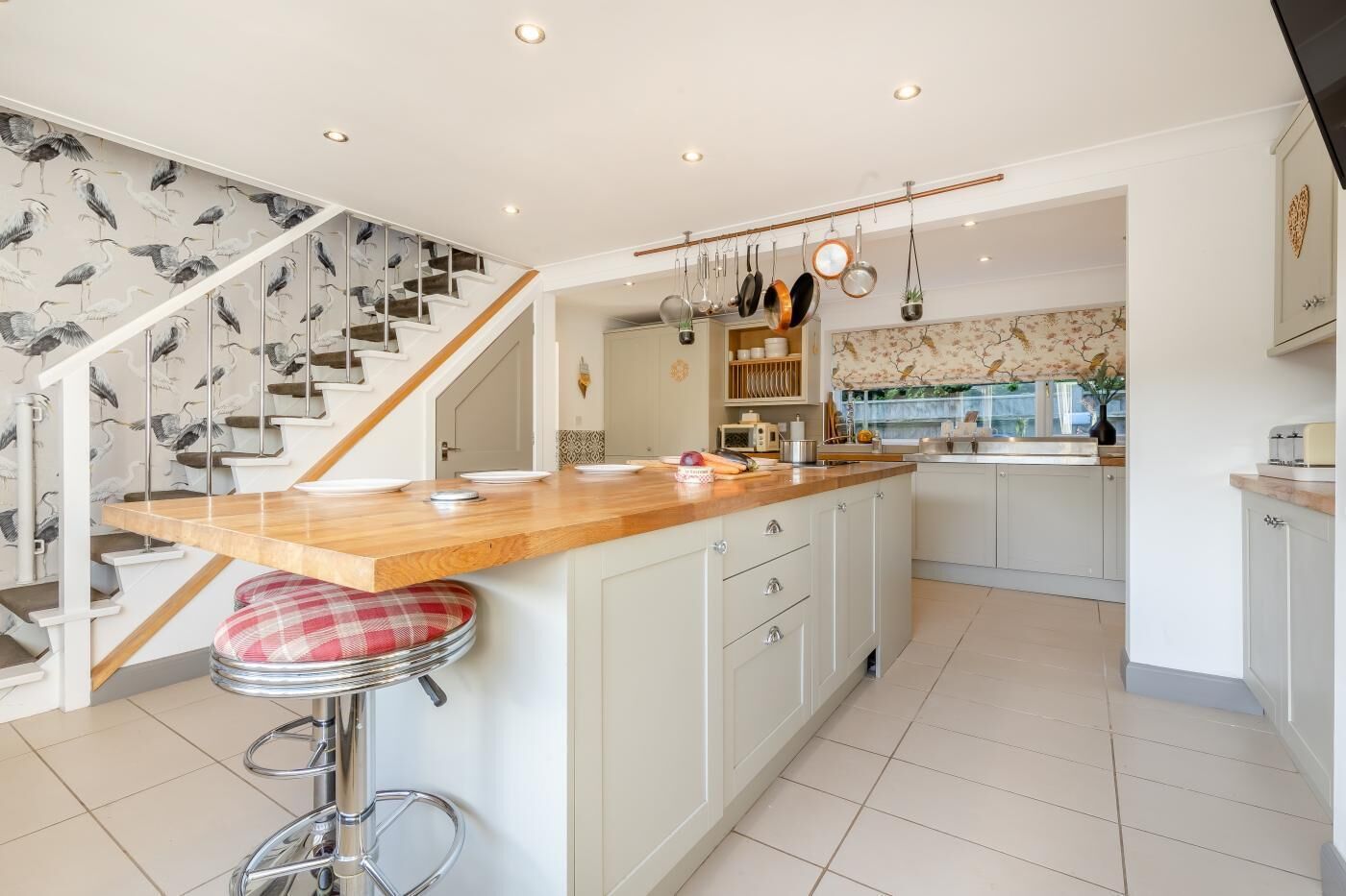 Een moderne keuken met een houten keukeneiland, roestvrijstalen apparatuur en een trap met een behang van vogelmotieven.
