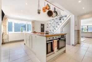 A modern kitchen with a central island, a built-in oven, and a hanging pot rack. - 5 Bed in Filby (oc-l30148) (Filby)