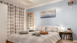 Un dormitorio con cama, mesitas de noche, lámpara, un cuadro y una estantería.