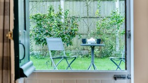 Vista desde una ventana a un patio con una mesa, dos sillas y un pequeño jardín.
