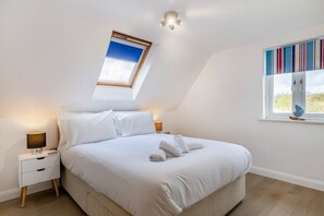 Quarto moderno com claraboia, cama com roupa de cama branca, mesa de cabeceira com luminária e janela com vista para o verde.
