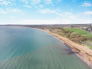 Vista costeira com praia, um cais e uma cidade ao fundo.