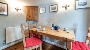 A dining area with a wooden table set for four, surrounded by chairs with red cushions. There are framed pictures on the wall, a wooden cabinet, and a radiator below the table. - 2 Bed in Castleton (oc-o30120) (Castleton)