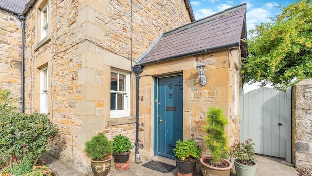 A stone building with a blue door, potted plants, and a grey gate. - 2 Bed in Aldbrough St. John (oc-l30130) (Aldbrough Saint John)