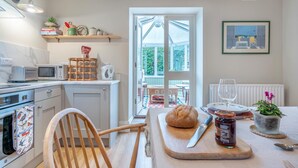 A modern kitchen with a wooden chair, a cutting board with bread and jam, and a dining table set for two. - 2 Bed in Aldbrough St. John (oc-l30130) (Aldbrough Saint John)