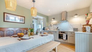 A modern kitchen with a dining area, featuring a wooden bench, a table set for a meal, and a hanging light fixture. - 2 Bed in Aldbrough St. John (oc-l30130) (Aldbrough Saint John)