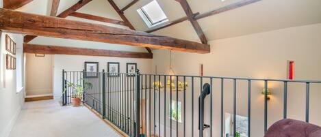 Un loft spacieux avec des poutres apparentes, un balcon doté d’une balustrade et une vue sur l’extérieur.