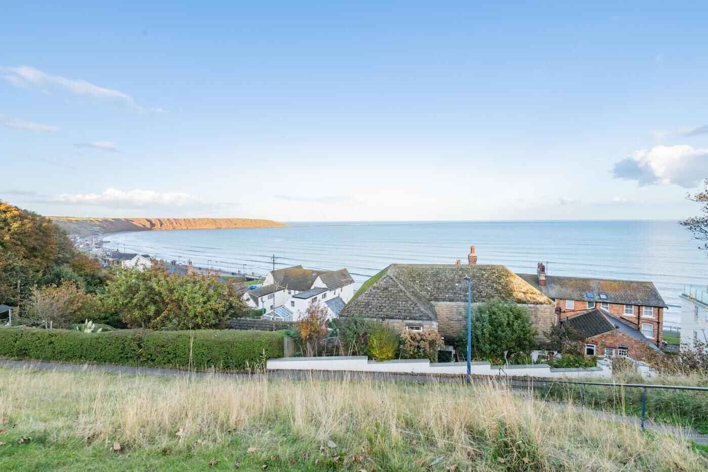 A coastal town with houses overlooking the sea, a clear sky, and a distant cliff.