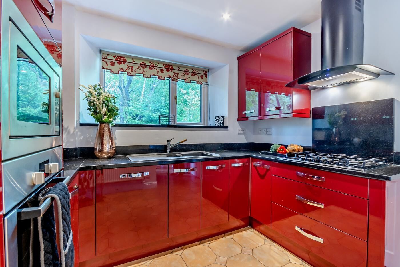 A modern kitchen with red cabinetry, a stainless steel stove, and a window with a view of trees.