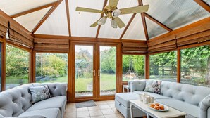 A conservatory with a wooden ceiling and glass doors, featuring a grey sofa, a small table with cups, and a view of a garden. - 3 Bed in Lea Bridge (oc-l30112) (High Peak Junction)