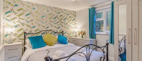 A bedroom with a bed, bedside tables, a dresser, a mirror, and a window with curtains.