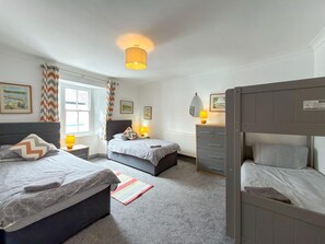 A bedroom with two beds, a dresser, a window with curtains, and a lamp. - 4 Bed in Tenby (oc-s30142) (Tenby)