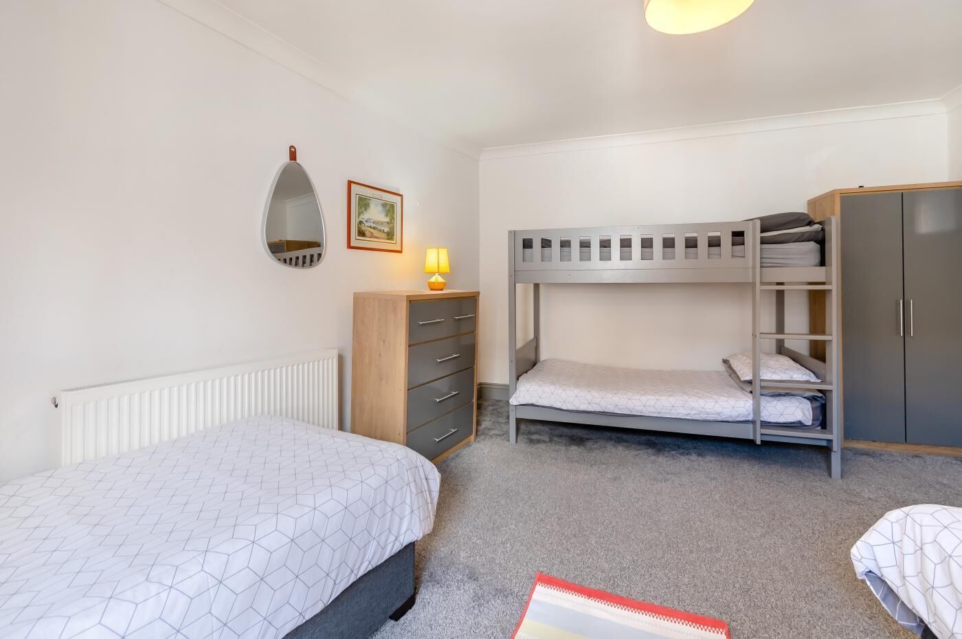 Une chambre avec un lit simple, une commode, une armoire et un lit superposé.