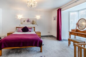 A bedroom with a bed, a dresser, a mirror, a chandelier, and a window with curtains. - 4 Bed in Tenby (oc-s30142) (Tenby)