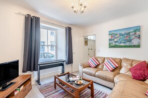 A living room with a leather sofa, a coffee table, a TV, and a painting on the wall. - 4 Bed in Tenby (oc-s30142) (Tenby)