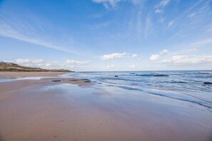 Ein Strand mit breitem Sandstrand, sanften Wellen und blauem Himmel.
