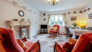 A traditional room with a fireplace, red armchairs, a dining table with a floral tablecloth, and a chandelier. - 2 Bed in Cresswell (oc-c30144) (Cresswell)