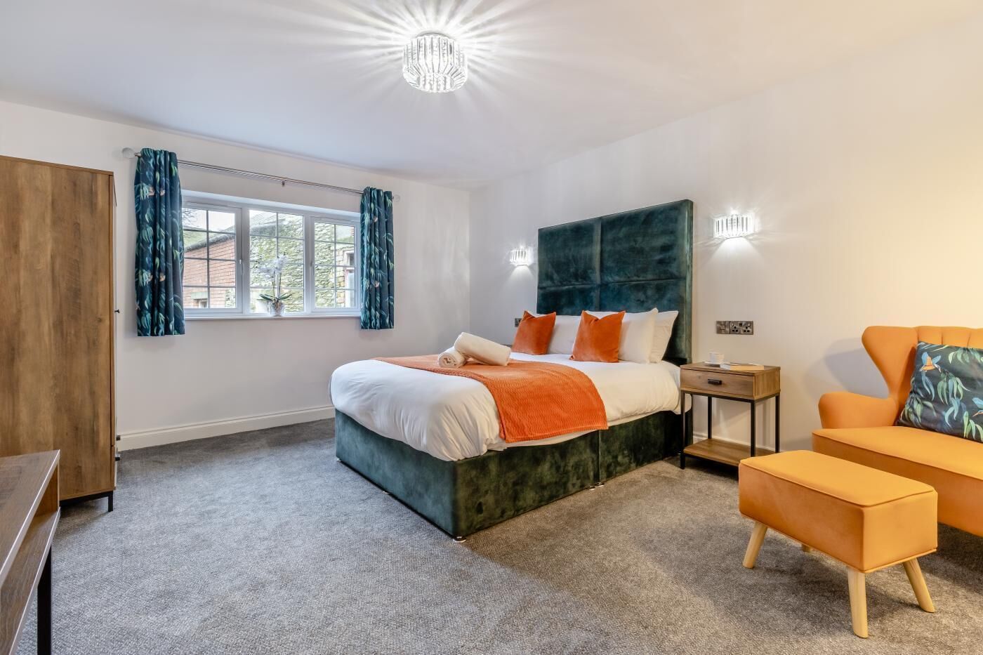 A modern bedroom with a large bed, a wooden wardrobe, a desk, and a sofa.