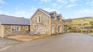 A stone building with a sloped roof, a paved driveway, and a small garden area with benches. - 2 Bed in Capel Bangor (oc-m30146) (Capel Bangor)