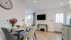 A modern dining area with a wooden herringbone floor, a dining table set with chairs, a vase of flowers, and a clock on the wall. - 2 Bed in Capel Bangor (oc-m30146) (Capel Bangor)