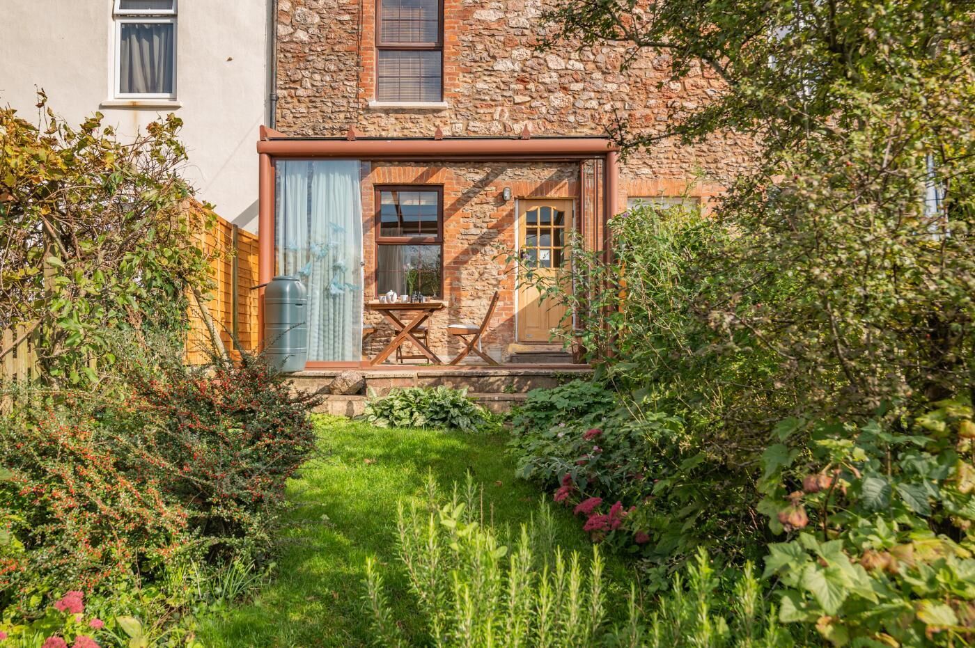 A stone house with a small garden, a wooden table, and a window.
