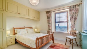 Een slaapkamer met een bed, nachtkastjes, een stoel, een dressoir en een raam met gordijnen.