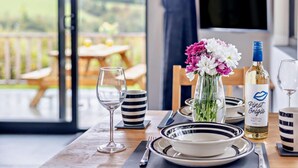 A dining table set with plates, bowls, and cutlery, a wine bottle, and a vase with flowers. - 1 Bed in Llanerfyl (oc-d30168) (Llanfair Caereinion)