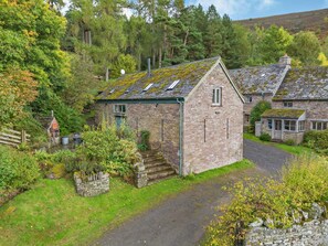 A stone cottage with a sloped roof, surrounded by lush greenery and a stone wall. - 2 Bed in Cwmdu (oc-l30162) (Cwmdu)