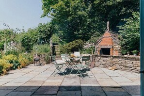 Eine Terrasse im Freien mit Steinboden, einem Backofen aus Ziegeln und einem Tisch mit Stühlen.