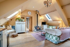 Ein Schlafzimmer im Dachgeschoss mit schrägen Wänden, Kamin, Bett, Fernseher und Dachfenster.