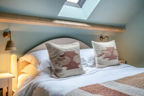 A bedroom with a skylight, a bed with white bedding, two decorative pillows, a bedside lamp, and a wall-mounted light fixture.