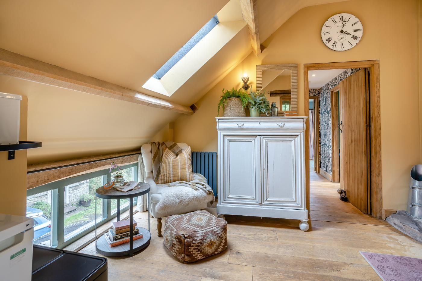 Ein gemütliches Schlafzimmer im Dachgeschoss mit Dachfenster, einem weißen Schrank, einem bequemen Sessel und einem kleinen runden Tisch mit Büchern.