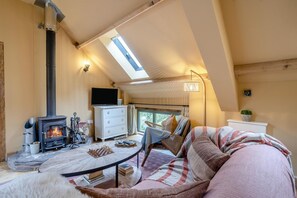 Ein gemütliches Zimmer mit Kamin, Fernseher, Sofa und einem Tisch mit Büchern.
