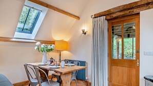 A cozy room with a wooden dining table, chairs, a vase of flowers, a lamp, and a view of greenery through a window. - 2 Bed in Cwmdu (oc-l30162) (Cwmdu)