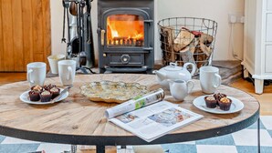 A cozy room with a wood-burning stove, a table set with tea cups, teapot, and pastries, and a basket of firewood. - 2 Bed in Cwmdu (oc-l30162) (Cwmdu)