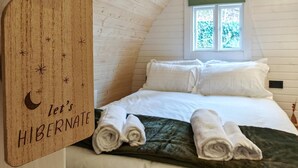 Ein gemütliches Schlafzimmer mit gewölbter Decke, einem Bett mit weißen Leinen und einem Holzschild mit der Aufschrift 'let's HIBERNATE'.