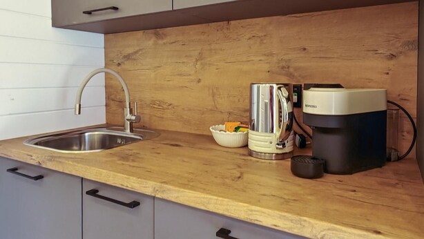 A kitchen with a stainless steel sink, wooden countertop, and a coffee machine.