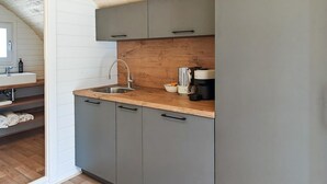 A kitchen with a wooden countertop, grey cabinets, a stainless steel sink, and a coffee maker.