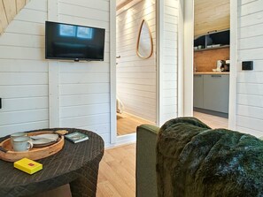 A modern interior with a flat-screen TV mounted on a white wall, a wooden dining table with a tray, and a cozy green chair. - 1 Bed in Pantygelli (oc-e30152) (Pantygelli)