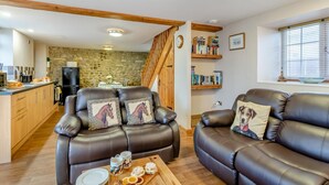 A cozy living room with leather sofas, a wooden coffee table with snacks, a kitchen in the background, and a staircase leading to another level. - 2 Bed in Thornton Watlass (oc-m30203) (Thornton Watlass)